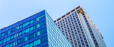 Looking up to the tops of two high rise office buildings ending below a blue sky