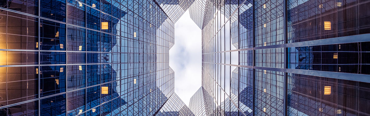 An upward looking view of towering glass office buildings creating a symmetrical, geometric pattern against the sky.